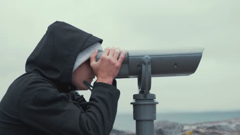 Young-man-looks-through-sightseeing-binoculars-bird-watching-spotting-at-scenic-landscape