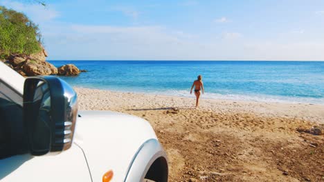 Car-in-the-foreground-with-a-girl-walking-in-bikini-towards-the-beach-in-the-background