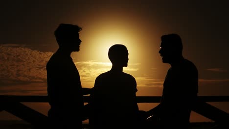Medium-long-shot-of-a-group-of-friends-having-a-discussion-along-a-boardwalk,-silhouetted-by-the-sunset