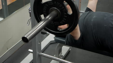 Joven realiza un ejercicio de press de banca con barra desde el pecho en el  gimnasio