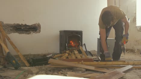young-man-chopping-sticks-with-hatchet-in-front-of-stove-while-renovating-house