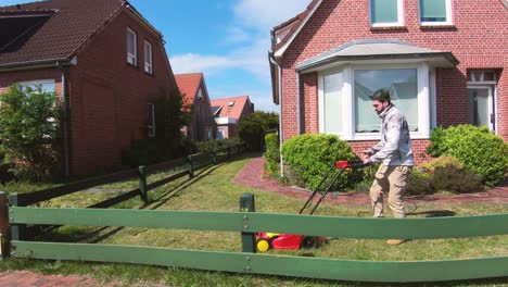 Young-man-cutting-the-grass-with-the-lawn-mower-in-front-of-the-house-next-to-a-fence