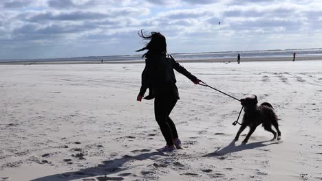 Girl-playing-with-the-dog-on-the-beach-on-a-sunny-windy-day-at-the-ocean