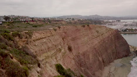 Aerial-footage-over-the-beautiful-red-cliffs-at-Dana-Point-in-San-Jan-Capistrano,-Orange-County,-California-revealing-the-harbor-and-Dana-Cove