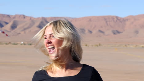 Close-up-of-a-joyful-blonde-girl-screaming-and-waving-her-hair,-background-mountains-in-soft-focus-SLOMO