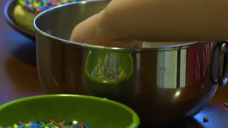 A-child's-hand-dips-a-homemade-cookie-into-icing-and-then-into-a-bowl-of-colorful-sprinkles