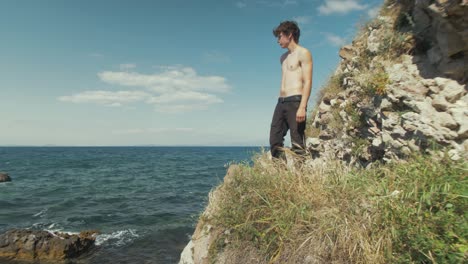 Young-shirtless-caucasian-male-stands-on-a-cliffside-overlooking-the-ocean