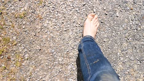 Walking-barefoot-along-gravel-road,-view-down-of-feet-and-denim-jeans