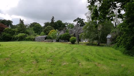 Old-Welsh-stone-cottage,-with-green-grass-and-trees-in-foreground,-STATIC
