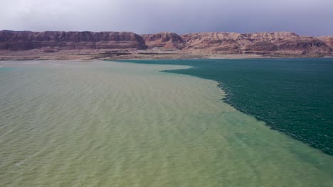 lot-of-muddy-water-from-flood-meet-the-dead-sea-water,-fly-over-the-muddy-water