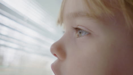 Close-up-of-a-blue-eyed-little-girl-looking-out-a-window-and-playing-with-the-blinds