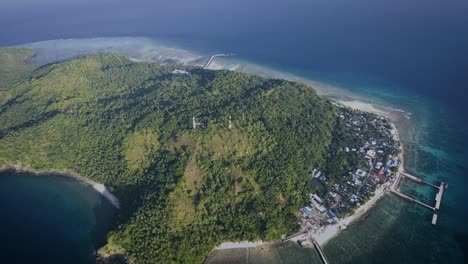 Aerial-shot-of-small-island-with-a-small-village-and-a-jetty,-surrounded-by-blue-ocean-in-the-afternoon