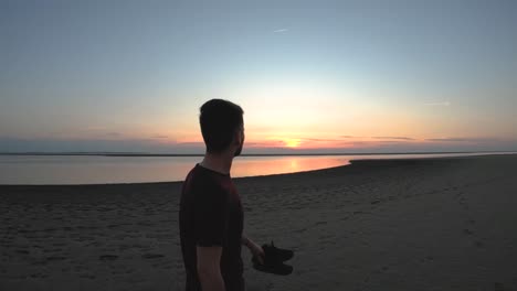 Man-walking-on-the-beach-with-the-sunset-and-the-ocean-in-front-of-him-slow-motion-close-up