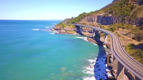 Las-Imágenes-Aéreas-De-Un-Impresionante-Puente-Largo-Y-Curvo-Junto-Al-Mar-Resaltan-El-Gran-Paseo-Pacífico-Con-El-Océano-Pacífico-Sur-Y-La-Vista-Del-Cielo-Azul-En-Un-Día-Soleado,-Sydney,-Australia