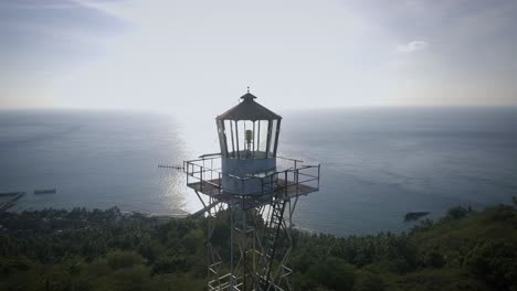 Aerial-shot-of-an-old-light-house-steel-tower-in-a-small-island,-backed-with-sunset,-surrounded-by-blue-ocean-in-the-afternoon
