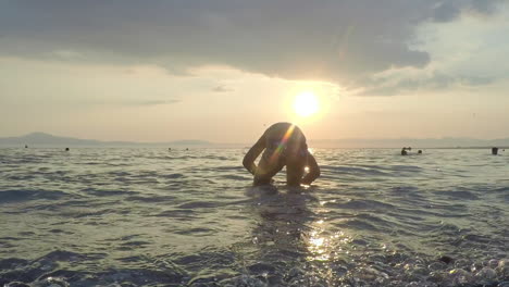 Kind-Spielt-An-Den-Wellen-Mit-Sonnenuntergang-Im-Hintergrund-Am-Strand-Von-Kalamata,-Griechenland
