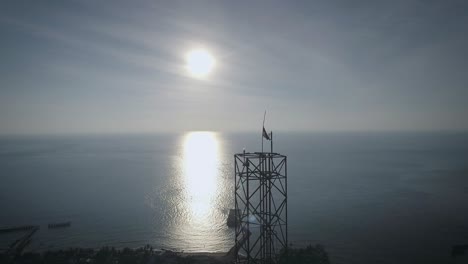 Aerial-shot-of-an-BTS-Base-Transceiver-Station-steel-tower-in-a-small-island,-backed-with-sunset,-surrounded-by-blue-ocean-in-the-afternoon