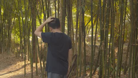 Walking-through-a-bamboo-grove-in-a-garden,-a-man-cannot-stop-scratching-his-itchy,-dandruff-scalp-on-his-balding-head