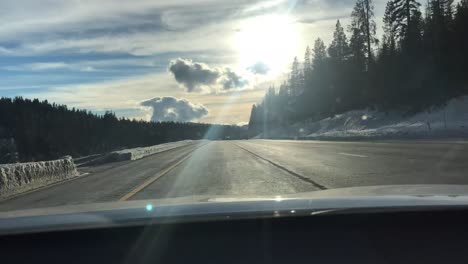 Time-lapse-shot-of-a-car-as-it-travels-down-a-country-highway-through-snowy-mountains,-sun-and-clouds,-other-vehicles-can-been-seen-in-the-adjoining-lanes