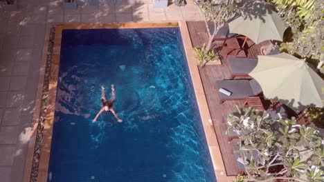 Disparo-De-Inclinación-De-Drones-Sobre-La-Piscina-Del-Hotel-Tropical-Con-Una-Joven-Nadando