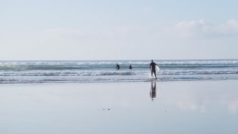 Surfers-walking-into-the-water-with-their-boards-under-their-arms