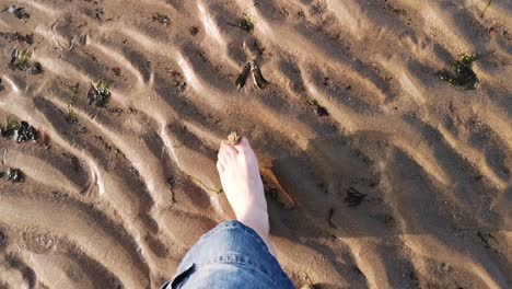 Walking-barefoot-across-the-beach,-with-sand-ripples-and-seaweed