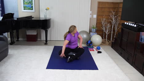 Older-woman-performing-twisting-stretches-cool-down-in-home-gym,-static,-locked-off