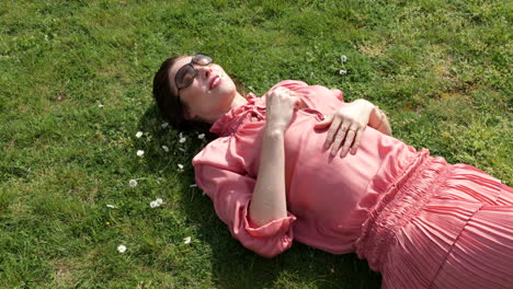 Schöne-Frau-Im-Rosafarbenen-Kleid,-Das-Sich-Im-Gras-In-Der-Sonne-Entspannt