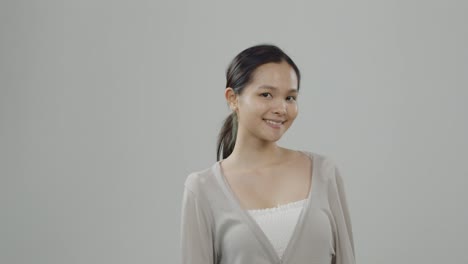 Cute,-young-Asian-woman-wearing-beige-sweater-over-white-shirt-and-no-makeup-poses-and-smiles-in-casting-audition---long-hair-pulled-back-in-a-ponytail