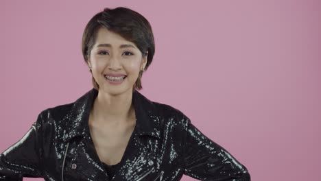 Young,-cute-Asian-wearing-black-jacket-smiles-and-poses-against-a-pink-backdrop-during-casting-audition