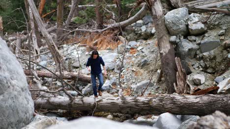 An-adult-caucasian-man-walking-along-a-fallen-tree-over-a-flowing-stream-in-the-forest-on-a-nature-hike