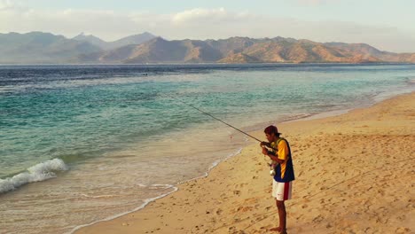 Young-man-fishing-on-an-exotic-beach-with-clear-skies-and-blue-water-in-the-exotic-holiday-location-of-Bora-bora