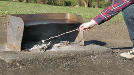 Woman-cooks-a-marshmallow-on-a-stick,-outdoors-on-open-coals