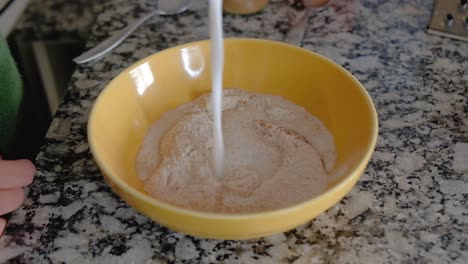 Woman-pouring-milk-over-dry-ingredients-on-a-bowl-to-form-a-batter