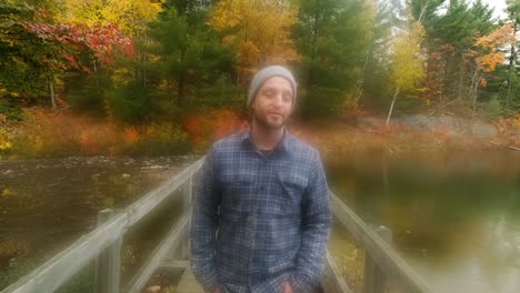 Man-Walking-on-Wood-Bridge-in-Colorful-Fall-Leaves,-Dreamy-Handheld-Track-Wide
