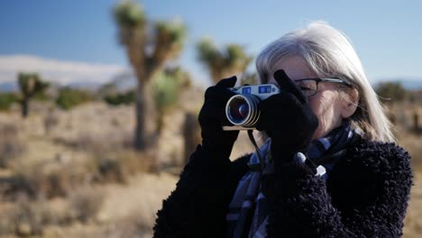 Eine-Erwachsene-Fotografin,-Die-Mit-Ihrer-Altmodischen-Filmkamera-In-Einer-Wüstenlandschaft-Fotografiert