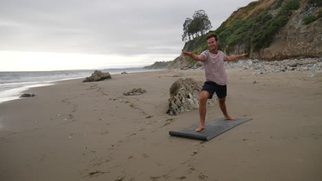 Ein-Glücklicher-Yogalehrer,-Der-Posen-Macht,-Während-Er-Am-Strand-Mit-Meereswellen-In-Zeitlupe-Lächelt