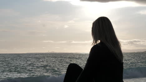 Sad,-blonde-woman-looking-out-to-the-sea-during-golden-hour