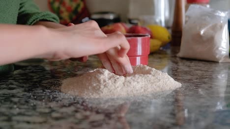 Woman-pouring-flour-over-the-countertop-and-making-a-hole-in-the-middle