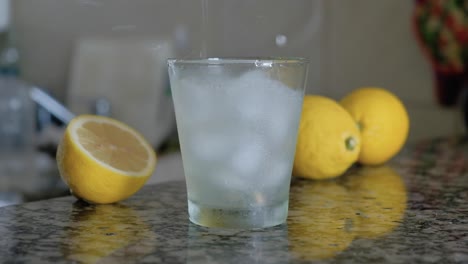 Limonada-Con-Cubitos-De-Hielo-Vertiéndose-En-Un-Vaso-Y-Salpicando-La-Encimera