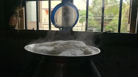 Topf,-Der-Reis-Auf-Traditionelle-Weise-Kocht,-Indem-Wasser-In-Einem-Schwarzen-Hintergrund-Gekocht-Wird,-Wobei-Weißer-Rauch-In-Zeitlupe-Kommt