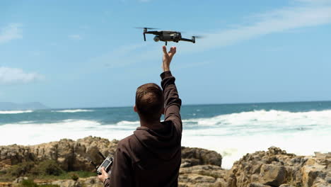 Man-catches-and-lands-drone-with-bare-hands,-ocean-in-background
