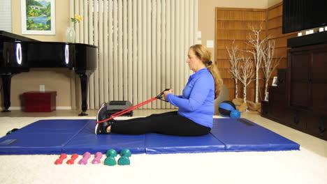 Woman-sitting-on-exercise-mat-using-stretch-band,-keep-fit,-home,-static