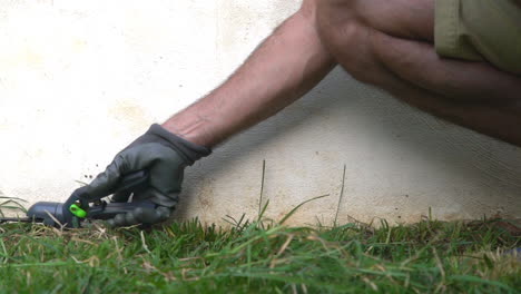 Footage-of-caucasian-male-gardener,-trimming-grass-with-scissors-pliers,-white-wall-background-120fps,-medium-shot
