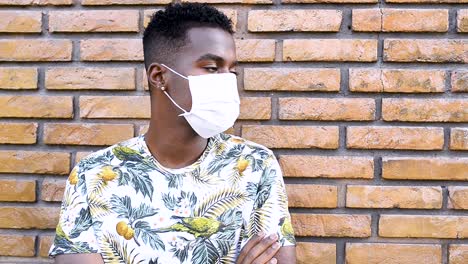 Afro-Brazilian-man-leaning-against-the-wall-with-covid19-coronavirus-mask,-depressed-and-anxious-with-arms-crossed