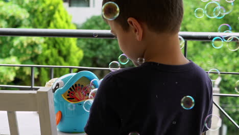 Slow-motion-shot-of-greek-toddler-boy-playing-with-a-soap-bubble-machine-at-the-balcony