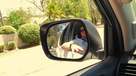 Man-looks-out-of-window-seen-in-rear-view-mirror-left-side-of-vehicle