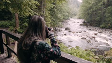 Slow-motion-shot-of-a-female-photographer-taking-photos-of-a-river-in-Vancouver-Lynn-valley,-Canada