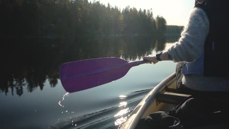 Woman-paddling-canoe-on-beautiful-lake-in-autumn,-rear-view-closeup-slow-motion
