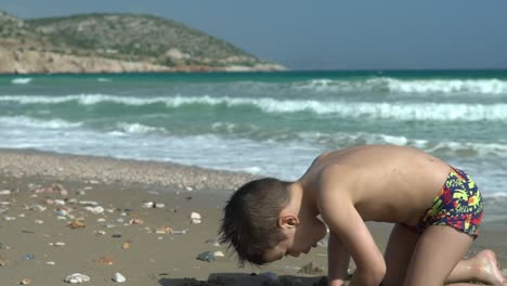 Caucasian-toddler-boy,-playing-with-sand-at-beach-of-Varkiza,-Greece